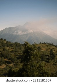 Mount merapi volcano in a hazy, cloudcovered sky with green leaves, creating a stunning natural landscape. Perfect for environmental and travel designs.