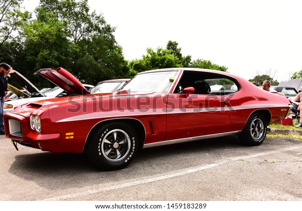 Mount Pleasant, Wisconsin\
/ USA - July 21, 2019: A red with white stripes 1972 Pontiac GTO\
with side fender vents at the Quarry Lake Car Show on a gloomy\
clouded afternoon .