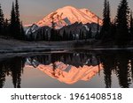Mount Rainier reflects in Upper Tipsoo Lake as alpenglow illuminates the volcanic peak with a mirror like reflection on a cold fall morning
