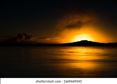 Mount Rangitoto sunrise daybreak artistic long exposure contrast light and dark scenic tourist destination sun rising over volcanic mountain and sea reflections calm tranquil mood