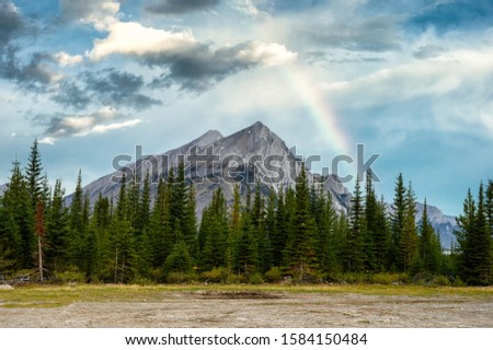 Mount Rundle with pine trees and rainbow in the blue sky at campground in provincial park