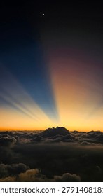 Mount Sumbing, Wonosobo, Central Java, Indonesia 31 july 2025

This photograph captures a breathtaking scene above a vast sea of clouds as dawn begins to break. Golden light emerges along the horizon, creating a stunning gradient that transitions from deep blue tones to warm shades of orange and gold. Dense cloud formations rise dramatically across the skyline, resembling majestic mountains floating above an endless ocean of clouds. Hidden just beyond the horizon, the sun casts radiant crepuscular rays upward into the sky, producing a mesmerizing and tranquil atmosphere. A delicate crescent moon hangs high above, adding a sense of serenity and wonder to the composition. The harmonious blend of light, shadow, clouds, and sky creates an extraordinary moment that showcases the grandeur of nature and inspires awe in those who witness it.