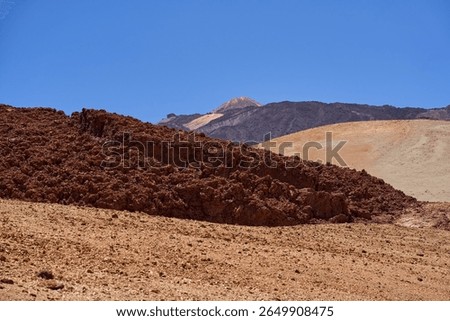 Mount Teide summit and cablecar station seen behind jagged dark lava fields under a clear summer sky