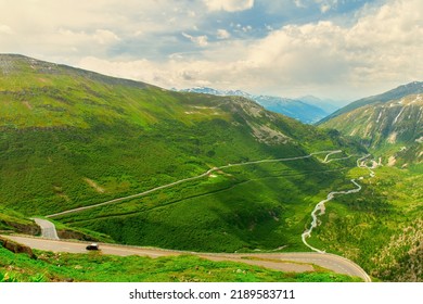 Mountain Alpine Landscape. Furka Pass In Swiss Alps In Summer. A Winding Serpentine Road Winds Among The Green Mountains, A Mountainous, Swift River Flows In The Valley,