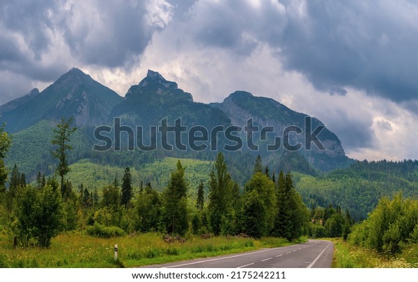Mountain asphalt road under\
high peaks without cars. Bicycle path in a mountain environment.\
Belianske Tatry (Tatry Bielskie), High Tatras, day with clouds.\
