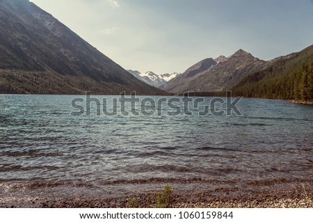 A mountain behind a blue lake. the shore of the lake with a pebble beach in the highlands