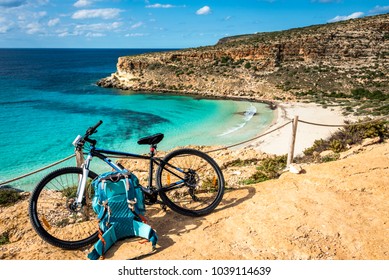 Mountain Bicycle And Blue Backpack, By The Sea. Rabbit Beach, Lampedusa, Sicily