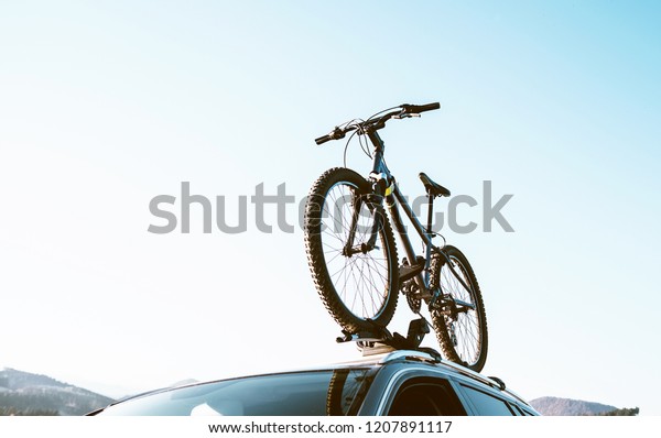 Mountain Bicycle fixed\
with Roof Mounted Bike Carriers instaled on white Auto roof travel\
concept image