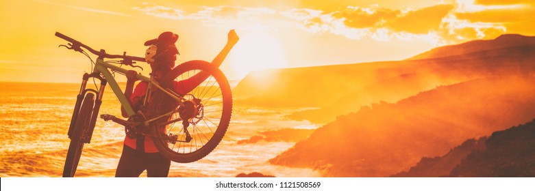 Mountain Bike Biking Cyclist Winning Race With Arms Up In Success, Achievement, Accomplishment And Winning. Happy Woman Cycling Raising Arms During Sunset Cheering At Trail Coast.