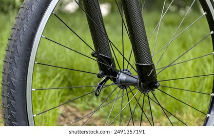 mountain bike fork and hub detail close up with green grass background (carbon aluminum rubber tire with black spokes) gravel wheel with quick release new build shiny - Powered by Shutterstock