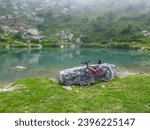 Mountain bike leaning to a stone next to small alpine lake along scenic mtb trail along ancient pathway from the Alps to the sea, through the Italian regions of Piemonte and Liguria, and France