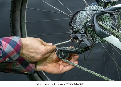 Mountain bike repair in the workshop. Mechanic's hand and rear derailleur close-up. Gearshift settings.