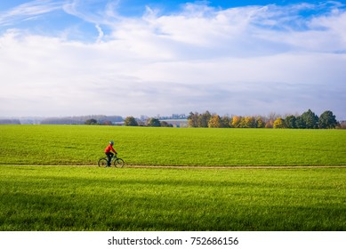 Mountain biker cyclist in countryside Zottegem, Flanders, Belgium. Mountainbike in motion riding through sunny grass field with trees in horizon. Fields in Autumn or fall in Flemish Ardennes, Belgium.