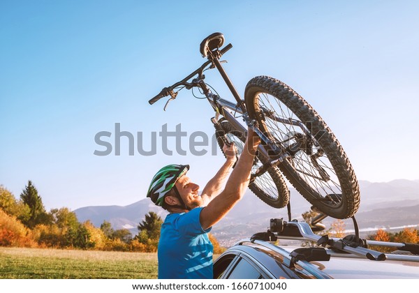 Mountain biker man take of his bike fronm\
the car roof. Active sport people concept\
image