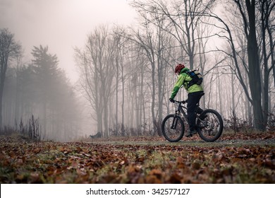 Mountain Biker On Cycle Trail In Woods. Mountains In Winter Or Autumn Landscape Forest. Man Cycling MTB On Rural Country Road. Sport Fitness Motivation And Inspiration.