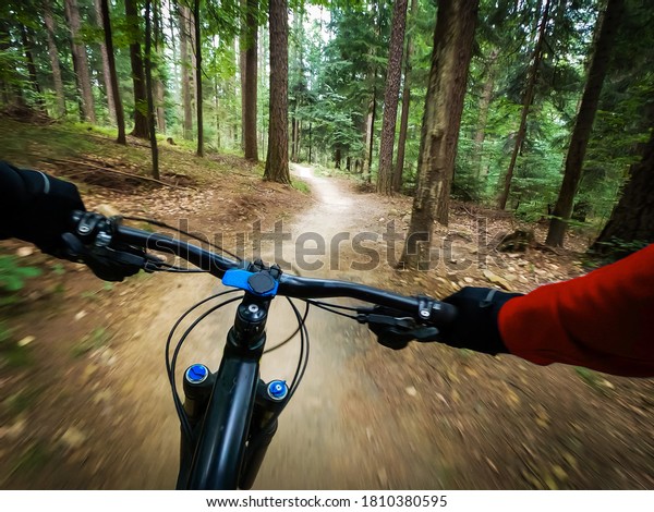 Mountain biker riding on\
flow single track trail in green forest, POV behind the bars view\
of the cyclist.