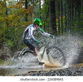 Mountain biker speeding through forest stream, water splash in freeze motion.
