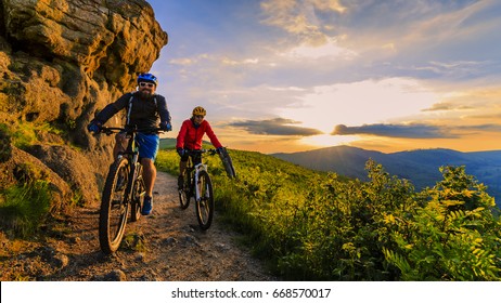 Mountainbike-Frauen und Mann, die auf dem Fahrrad bei Sonnenuntergang Berge Waldlandschaft fahren. Mehrere Radfahrer MTB Enduro-Flussweg. Sportliche Aktivitäten im Freien.