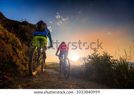 Mountain biking women and man riding on bikes at sunset mountains forest landscape. Couple cycling MTB enduro flow trail track. Outdoor sport activity.