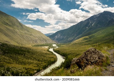 A Mountain Breathtaking River Flows Through The Tranquil Plain Under The Large Clouds Somewhere In The Mountains, Aerial Panoramic View With No People