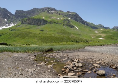 Mountain brook or stream opening into a dried up lake. There is very little  water in the brook and the lake bottom is exposed because there is no water. Region Melchsee-Frutt in Switzerland. - Shutterstock ID 2205985049