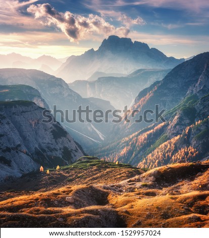 Mountain canyon lighted by bright sunbeams at sunset in autumn in Dolomites, Italy. Landscape with mountain ridges, rocks, colorful trees and orange grass, alpine meadows, gold sunlight in fall. Alps