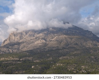 mountain capped by low clouds, towering monolith with craggy cliffs and textured granite face, dramatic light