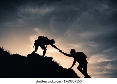 Mountain climber helping fellow climber up rocky edge of a mountain cliff. Never give up, and helping hand concept.  - Shutterstock ID 1963807153