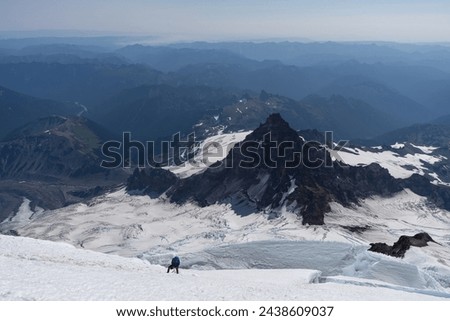 Mountain Climber standing on a Glacier on Mount Rainier, looking out over the peaks and valleys of the Cascade Range