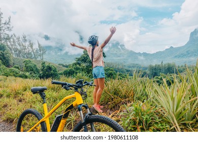 Mountain e biking happy girl with arms up of happiness traveling on Tahiti island with e-bike riding electric mtb bicycle on trail adventure. Travel summer lifestyle. - Shutterstock ID 1980611108