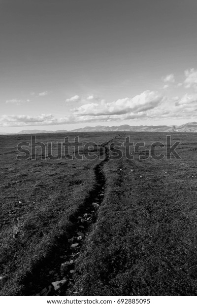 A mountain field
with a very long crack going toward the horizon, beneath a deep sky
with white clouds