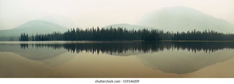 Mountain and forest over lake with reflections in a foggy day.