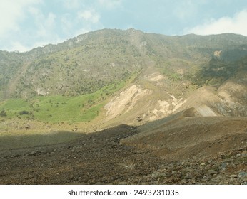 A mountain with a green hillside and a rocky, barren hillside. The sky is clear and the sun is shining - Powered by Shutterstock