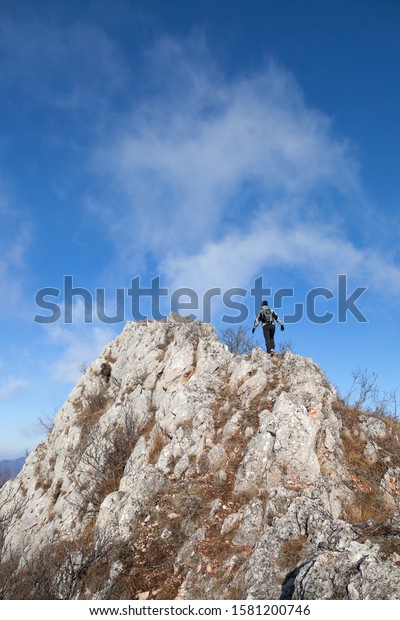 Mountain hiker with hood,\
backpack and gloves walking over narrow, dangerous, rocky mountain\
ridge