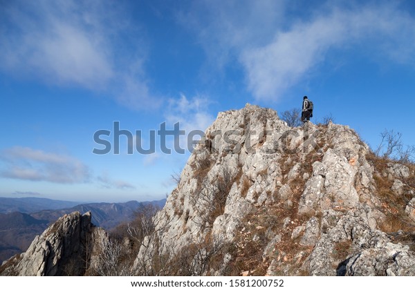Mountain hiker with hood,\
backpack and gloves walking over narrow, dangerous, rocky mountain\
ridge