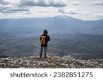 Mountain hiker with orange backpack standing at the edge of the cliff and looking at Suva planina (Dry mountain) and snow covered Trem summit