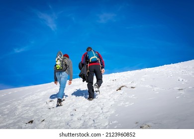 Mountain Hikers Climb To The Snowy Peak, Blue Sky In The Background.