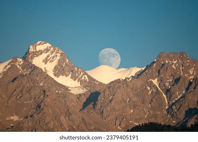 A mountain landscape with an almost full moon. Komsomol Peak (Nursultan) and Karlytau peak. The Alatau Ridge on the Tien Shan. Almaty, Kazakhstan