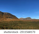 A mountain landscape with autumn foliage in Sweden. Dense forest covers the lower slopes, while the peaks rise under a clear blue sky, showcasing vibrant fall colors in the trees.