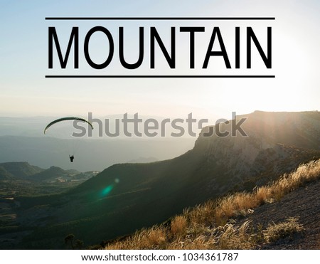 Mountain landscape background at sunset with person doing paragliding, with the word Mountain written on top. Concept Advertising.