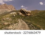 Mountain landscape  - country road with big yellow rounded boulder in bright sunny summer day with pink rocky ridge of mountain away and green grass meadow, blue sky. Trekking in Dagestan mountains.