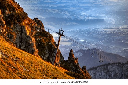 Mountain landscape at sunrise with cable car system on a rocky slope and a misty valley in the background.  - Powered by Shutterstock