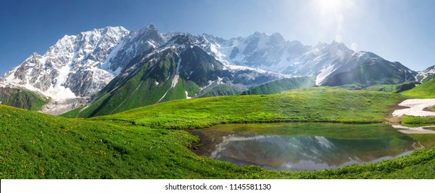 Mountain landscape of Svaneti on bright summer sunny day. Mountain lake, hills covered green grass on snowy rocky mountains background. Caucasus peaks in Georgia. Amazing view on wild georgian nature - Powered by Shutterstock