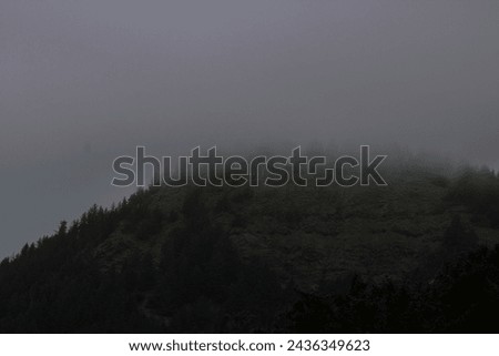 A mountain looms through thick fog, its silhouette cloaked in mystery, evoking a sense of awe and curiosity.
