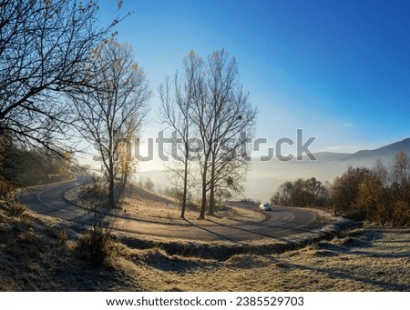 mountain pass in autumn. sun behind the leafless trees on the grassy hills in frost. mist in the valley. blue sky above the distant ridge