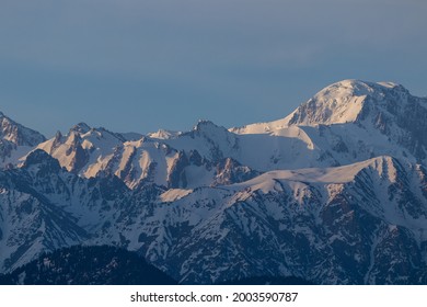 Mountain peak with blocks of ice and sharp rocks in the snow illuminated by the sun at sunrise. Against the blue sky