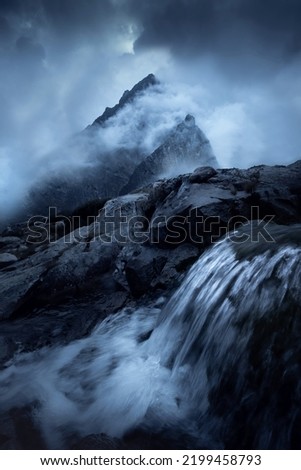 Mountain peaks in the clouds with a waterfall in the foreground. High Tatras in Slovakia
