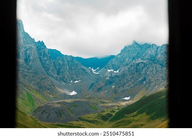 Mountain Peaks Framed by Window View
Stunning mountain peaks with patches of snow, viewed through a window frame on a cloudy day, capturing natural beauty.
 - Powered by Shutterstock