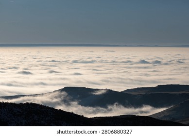 mountain peaks pierce through cloud layers. Calm sky overlooks endless cloud sea below. Misty atmosphere enhances serene landscape. Ideal for nature travel and meditation themes