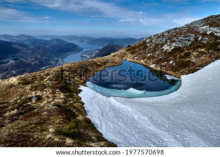 A mountain pond with snow around. Hiking the mountains Skåldalsnipa (603 meter), Skåldalsfjellet (718 meter), Herlandsfjellet (696 meter) and Garnesrinden (625 meter) in Bergen, Norway